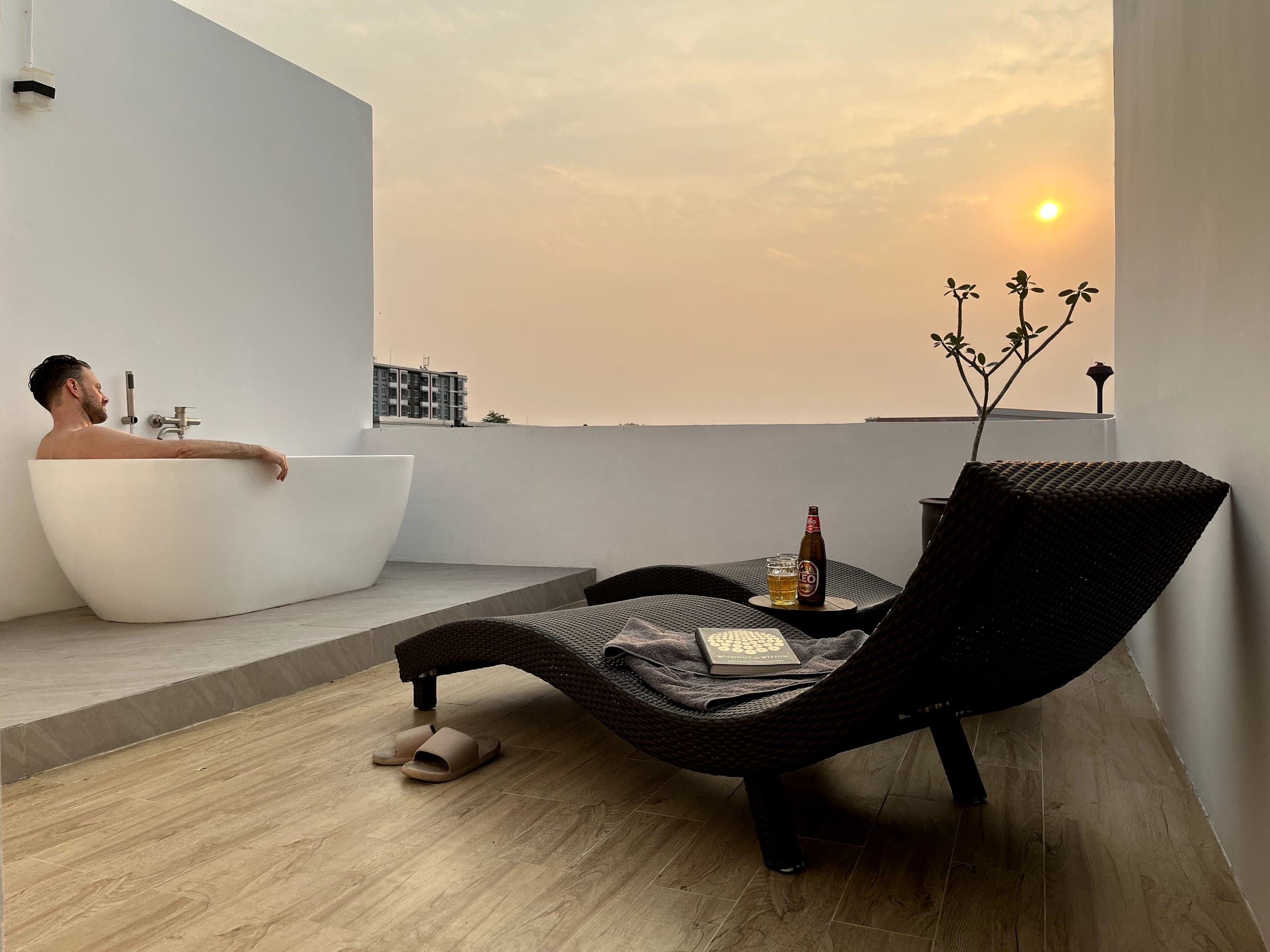 The soaking tub and a wicker lounger on the roof terrace at sunset